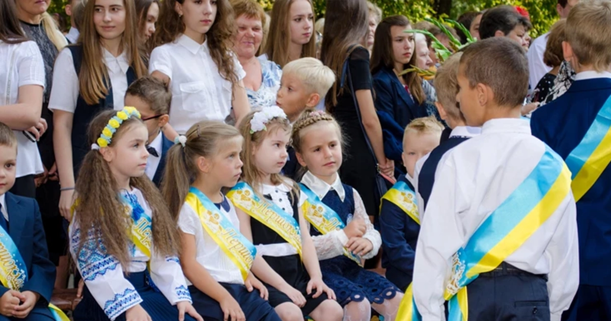 Дитина з рюкзаком, яку фотографують на шкільному подвір’ї